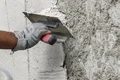 Une main applique de l'enduit à la truelle sur un mur extérieur, projet Baumit DIY destiné aux bricoleurs.