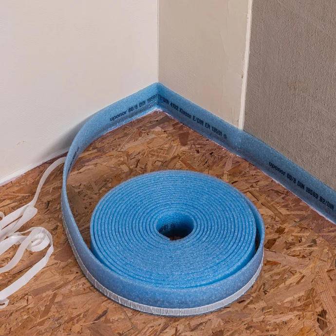 Angle intérieur d'une pièce : vue détaillée de la bande d'isolation périphérique en rouleau. La bande d'isolation périphérique est fixée dans l'angle.