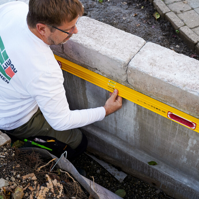 Der Handwerker zeichnet die Position des Protektor Noppenbahn-Profils mit einer gelben Wasserwaage an der Mauer an.