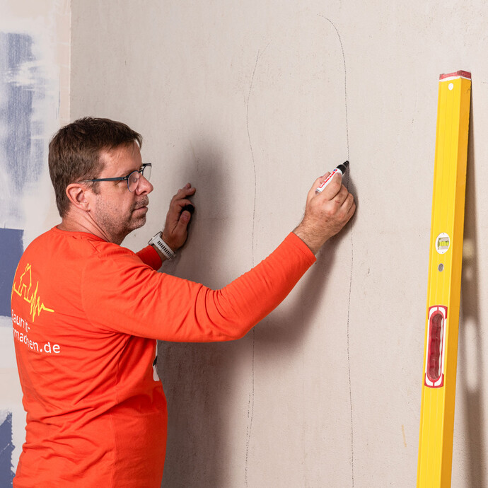 Heimwerker markiert mit einem Edding die problematischen, unebenen Stellen an der Wand.