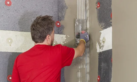 Un bricoleur applique de l’enduit sur un mur isolé à l’aide d’un enduit de lissage ; instructions étape par étape pour l’isolation de façade avec les produits Baumit.