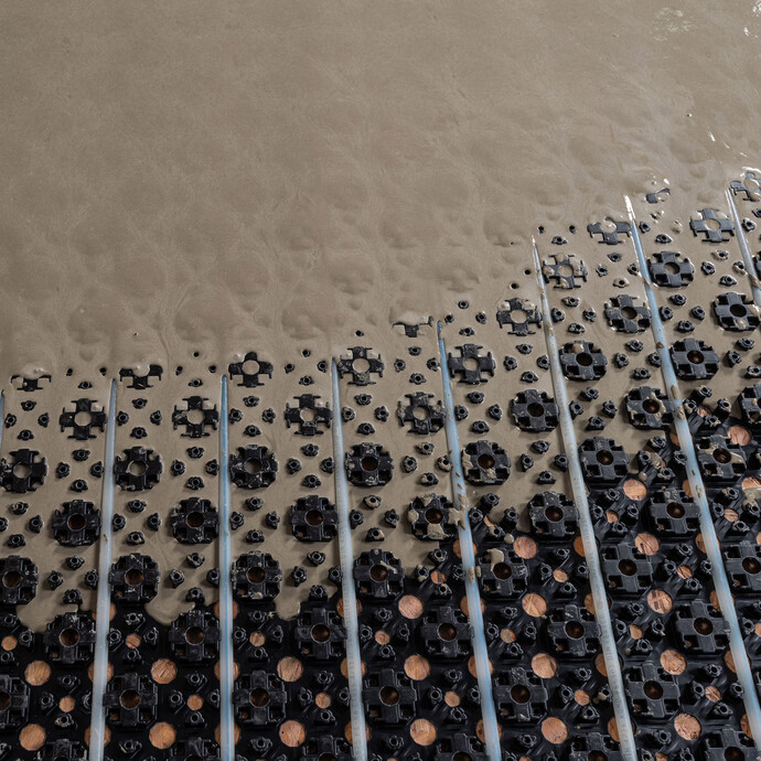 Photo de détail : Plaque à plots avec tuyaux de chauffage - la masse d'égalisation auto-nivelante remplit entièrement la plaque à plots.