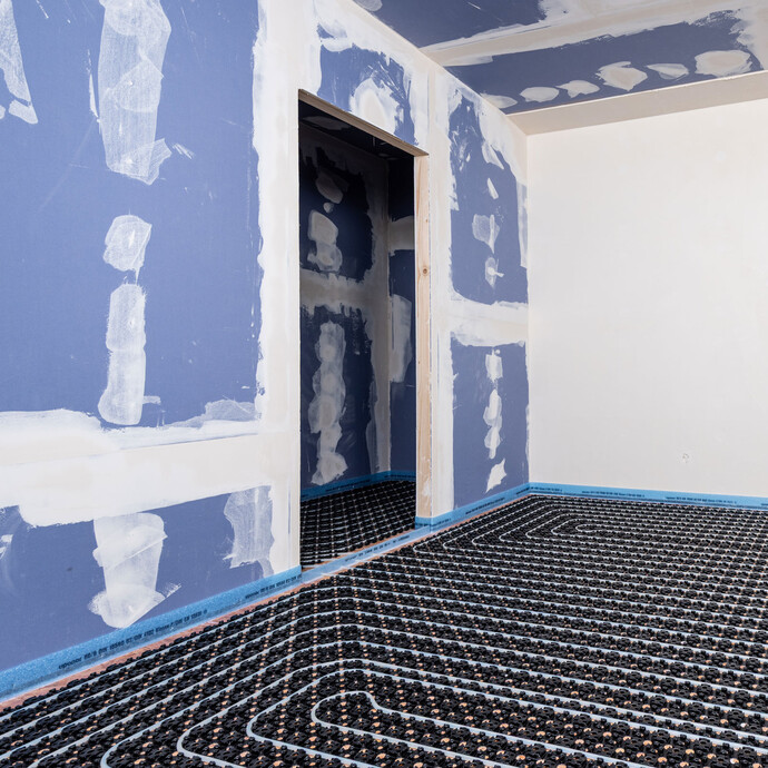 Rénovation d'un bâtiment ancien : pièce avec des cloisons sèches et un chauffage au sol à eau déjà installé.