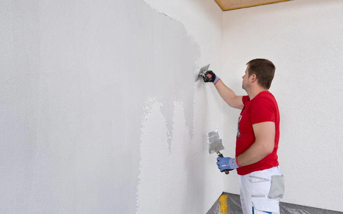 Heimwerker trägt glatten Putz mit einer Kelle auf eine Innenwand auf.
