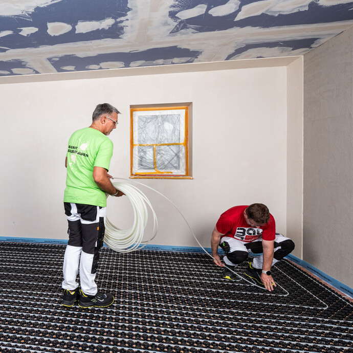 Deux ouvriers posent le tuyau de chauffage du chauffage par le sol Minitec dans les plaques à plots. La première personne tient le tuyau, la seconde pose le tuyau de chauffage.