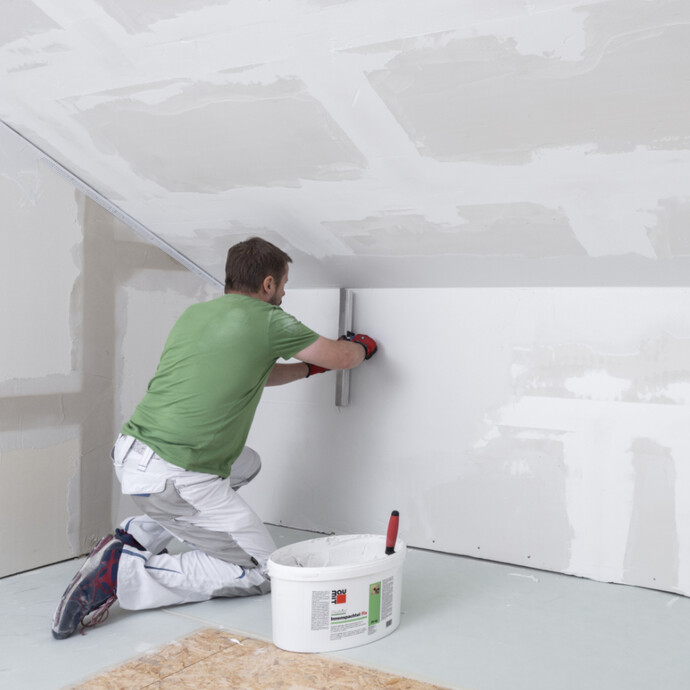 frische, weisse Spachtelmasse mit einem breiten Flächenspachtel an der Wand eben abziehen