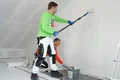 L'enduit au silicate Airless et au rouleau est appliqué par une personne à l'aide d'un rouleau, tandis qu'une autre personne lisse l'enduit.