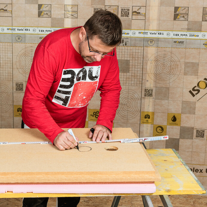 Der Baumit Heimwerker überträgt die ermittelten Maße der Kabeldurchführung auf der Rückseite der Holzfaserdämmplatte und den Kabelverlauf zur Gerätedose.