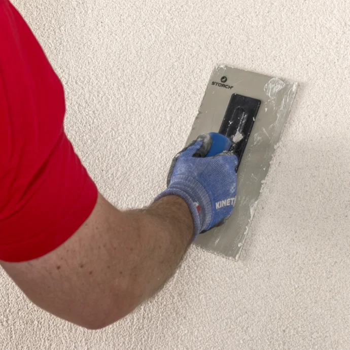 Person trägt Putzschicht mit Kelle auf Wand auf.