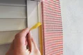 Hand zieht Abdeckband von Fensterrahmen neben montiertem Armierungsgewebe für Putzarbeiten.