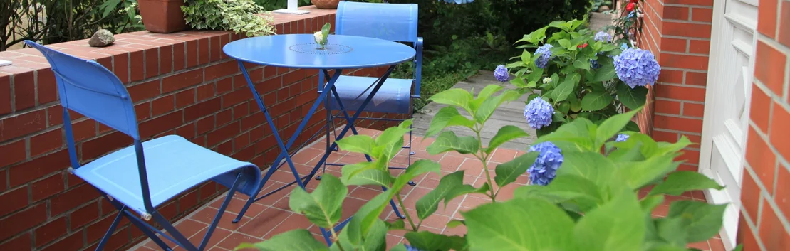 Gem&uuml;tliche Backsteinterrasse mit blauen Gartenm&ouml;beln und bl&uuml;henden Hortensien f&uuml;r Heimwerkerideen und Gartengestaltung.