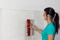 Frau strukturiert frisch aufgetragenen Putz an der Wand mit Bürste für dekoratives Finish.