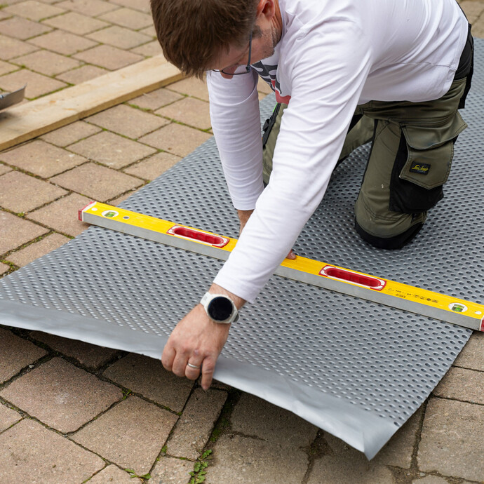 Handwerker kniet auf der Noppenbahn mit einer gelben Wasserwaage, um die Noppenbahn vorzuknicken.