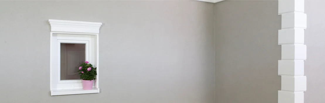 Graue Innenwand mit wei&szlig;em Fensterrahmen und einer Pflanze in einem rosa Topf auf der Fensterbank.