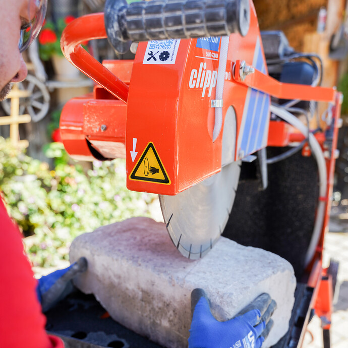 Heimwerker richtet den Mauerstein auf der Tischsäge Norton Clipper so aus, dass das Sägeblatt exakt auf der Schnittlinie ist.