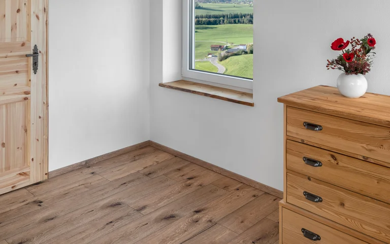 Parquet en bois et commode en bois dans une pièce lumineuse avec fenêtre et vue sur le paysage, source d’inspiration pour des projets de bricolage.