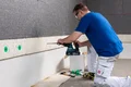 Heimwerker befestigt Dämmplatten mit Akkuschrauber an der Wand, um Energieeffizienz zu steigern.