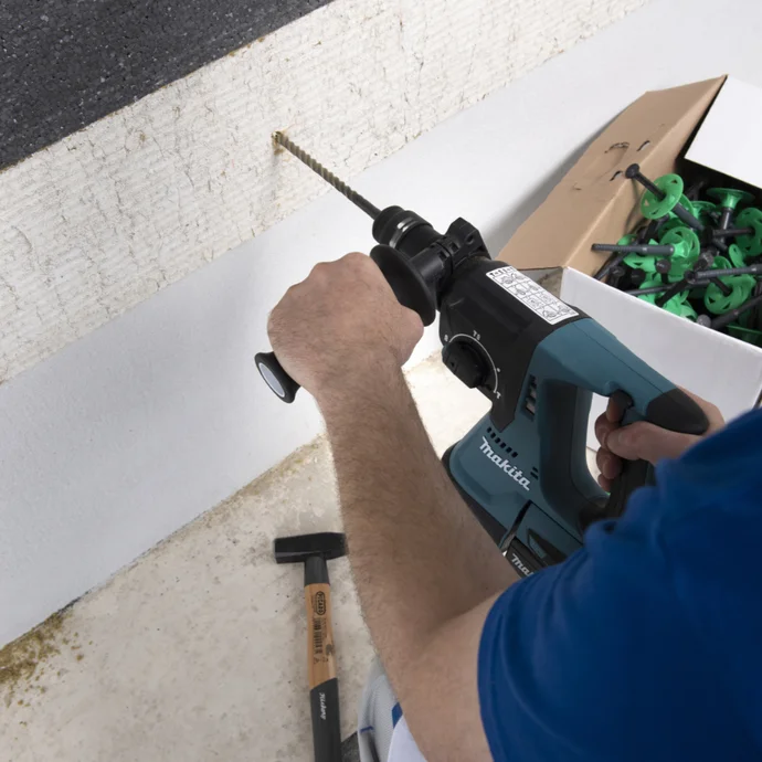 Une personne perce un mur, des outils sont disposés à côté.