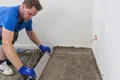 Mann beim Bodenverlegen: Estrich mit Richtlatte glattziehen für gleichmäßige Oberfläche in modernem Wohnraum.