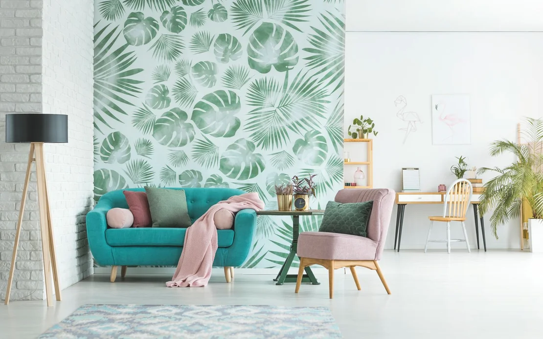Modernes Wohnzimmer mit gr&uuml;ner Bl&auml;ttertapete, t&uuml;rkisfarbenem Sofa, rosa Stuhl und Schreibtisch im Hintergrund.