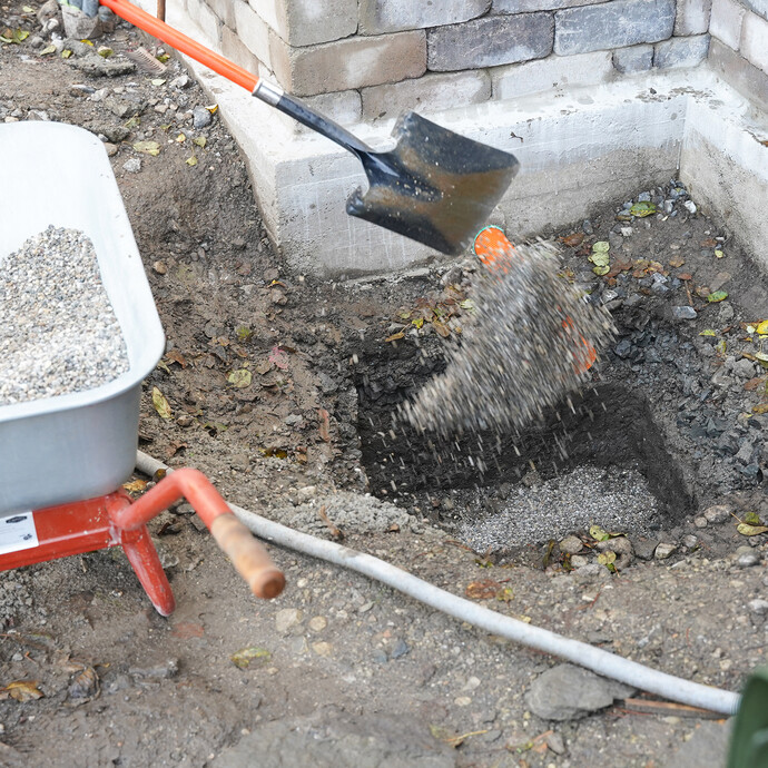 Detailfoto: Kies wird mit Hilfe einer Schaufel in die Grube für die Sickerbox gefüllt.
