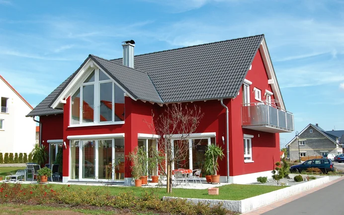Modernes rotes Haus mit Dachziegeln, großen Fenstern und Balkon, perfektes Beispiel für gelungene Fassadengestaltung.