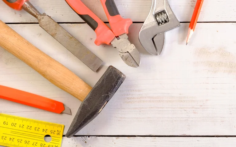 Werkzeuge für Heimwerkerprojekte: Hammer, Zange, Schraubenschlüssel, Bleistift, Maßband und Feile auf Holztisch.
