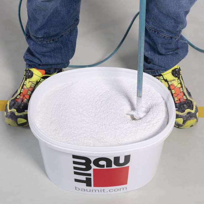 Pastöser Strukturputz im Baumit-Eimer wird mit einem elektrischen Rührwerk aufgemischt.