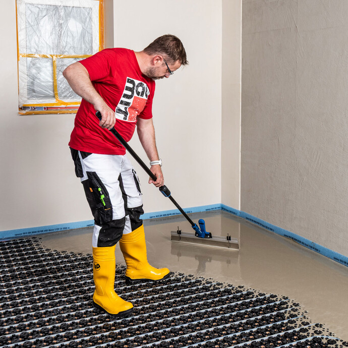 Heimwerker verteilt die selbst nivellierende Ausgleichsmasse mit Hilfe eines Rakel.