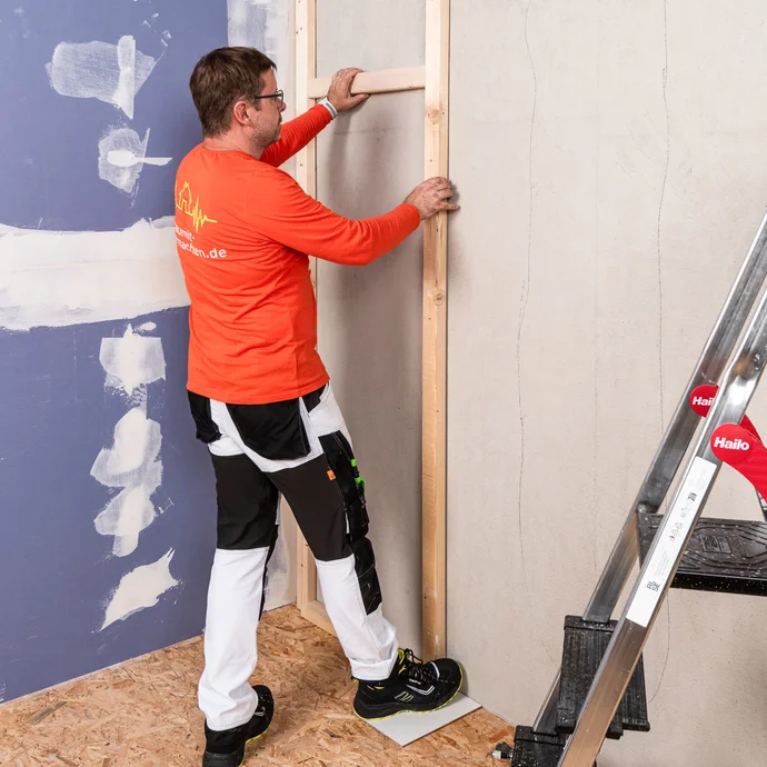 Heimwerker verwendet ein zweites Abstandsholz, das er als Abstandslehre nutzt. So können die weiteren Kanthölzer schnell und einfach an der Wand befestigt werden. Du sparst dir damit Zeit und musst nicht immer erneut aufwändig ausmessen.