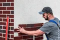 Heimwerker bringt Verblendsteine an Hausfassade an, Schritt-für-Schritt-Anleitung für Bauprojekt.