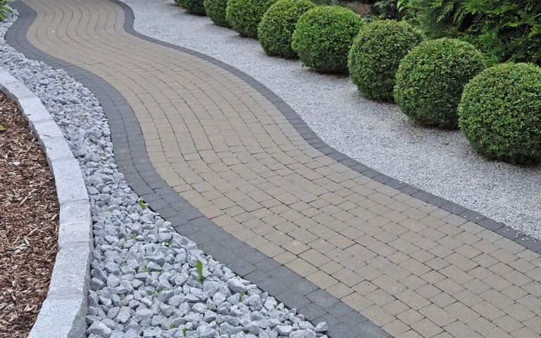 Gepflasterter Gartenweg mit dekorativen Randsteinen und Kiesbeeten, ideal zur Verschönerung von Außenanlagen.