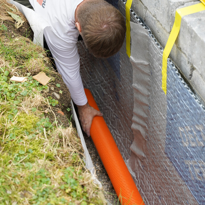 Handwerker verlegt ein Drainagerohr auf dem Filterkies an der Gartenmauer.