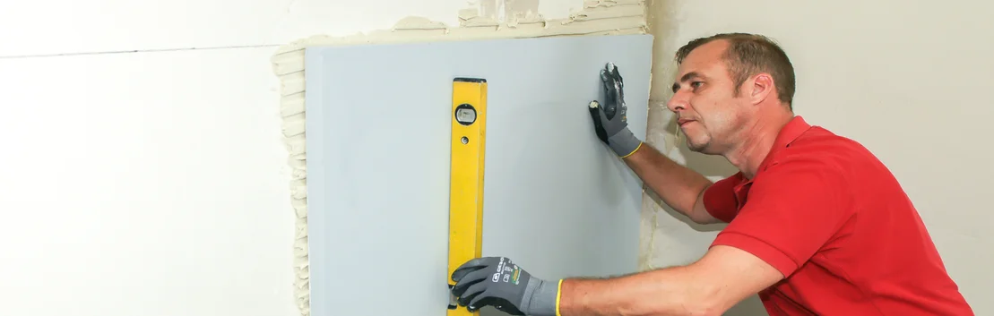 Handwerker gleicht mit einer Wasserwaage eine Wand aus, um eine pr&auml;zise Montage von Trockenbauplatten zu gew&auml;hrleisten.