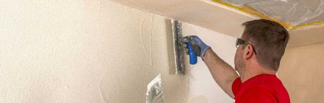 Heimwerker mit Kelle gl&auml;ttet wei&szlig;en Putz an Wand und Decke f&uuml;r ein sauberes Finish, Baustelle im Innenbereich.