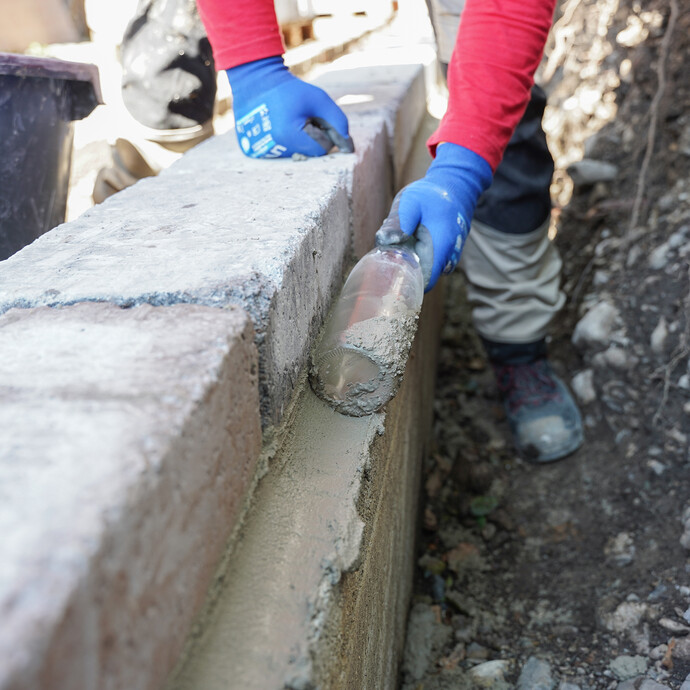 Eine Person formt mit einer Flasche eine Hohlkehle an der Mörtelfuge der Gartenmauer.