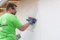 Le bricoleur applique l'enduit fouetté de Munich sur la façade à l'aide d'une truelle.