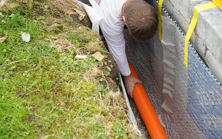 Handwerker verlegt ein Drainagerohr auf dem Filterkies an der Gartenmauer.